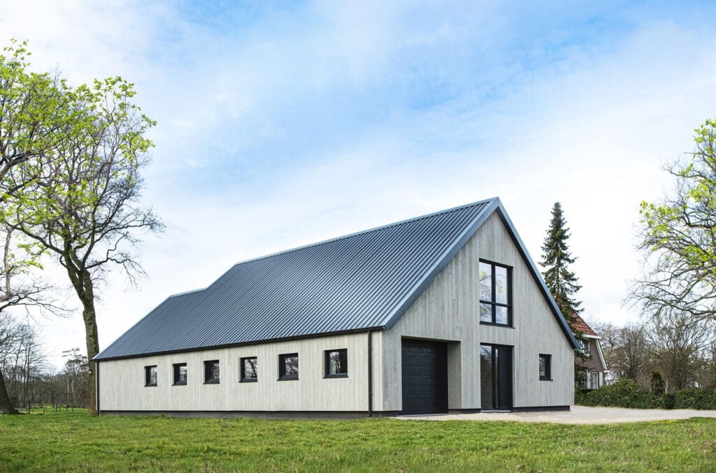 Een moderne schuurwoning met een metalen dak en strakke Millboard gevelbekleding, omgeven door een groene omgeving.