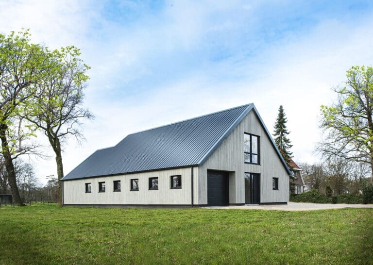 Een moderne schuurwoning met een metalen dak en strakke Millboard gevelbekleding, omgeven door een groene omgeving.