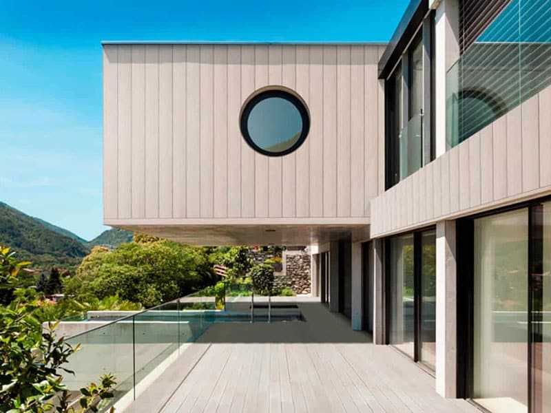 Een modern huis met een zwevend bovenste gedeelte en een rond raam, gelegen in een groene heuvelachtige omgeving onder de heldere blauwe lucht.