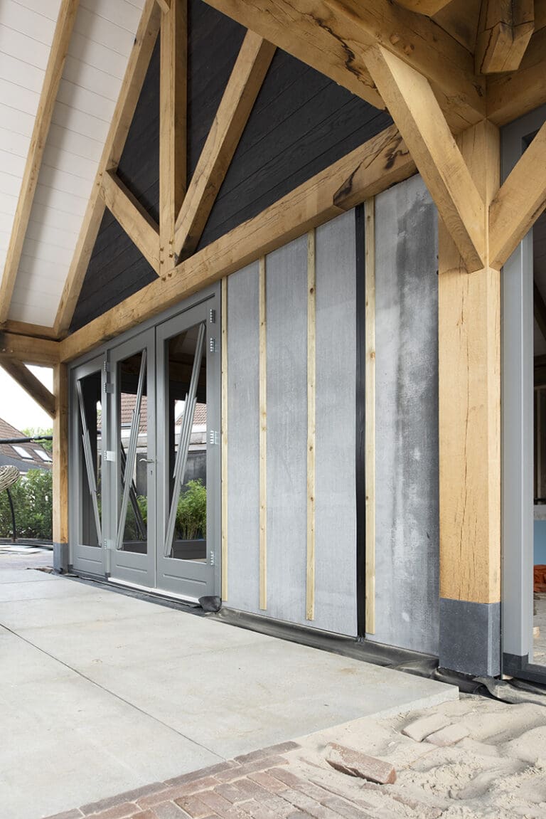 Een woning in aanbouw met houten balken, zwarte planken en geïnstalleerde gevelplaten.