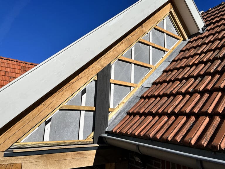 Een dakconstructie met rode dakpannen en houten balken, waarbij wettershield planken worden geïnstalleerd. Op de achtergrond is een heldere blauwe lucht.