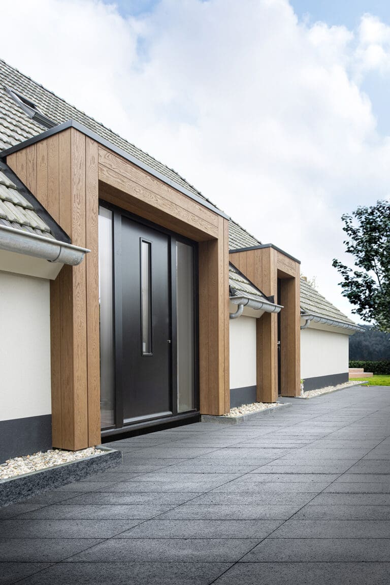 Een modern gebouw met een combinatie van Millboard gevels en wit geschilderde muren, zwarte deuren en ramen, en een dak met grijze dakpannen.
