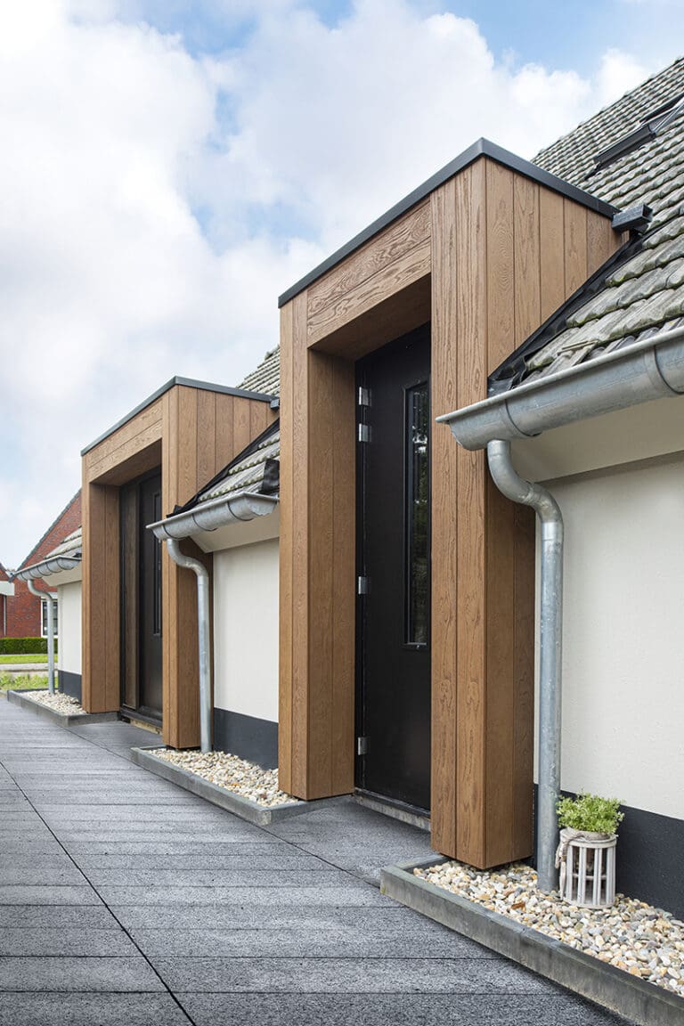 Een modern gebouw met een combinatie van Millboard gevels en wit geschilderde muren, zwarte deuren en ramen, en een dak met grijze dakpannen.