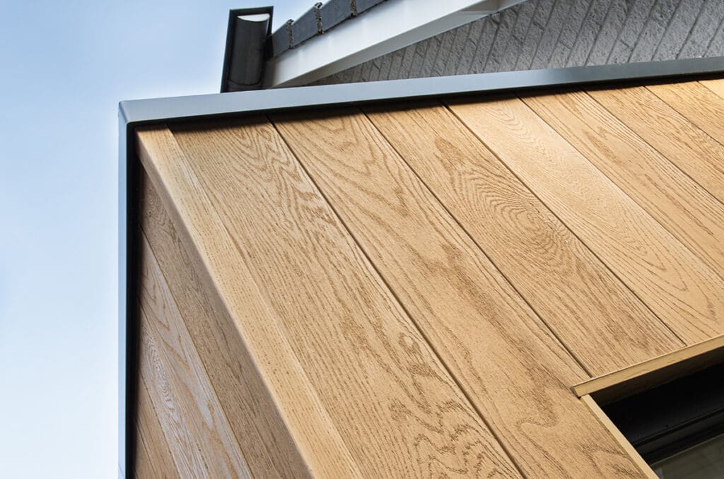 Een modern huis met een uitbreiding in lichte Millboard afwerking, zwarte ramen, en een grijs pannendak. Het originele huis heeft lichte bakstenen muren.