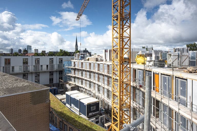 Een bouwplaats in Rotterdam waar een gevelpaneel van magnesiumoxide wordt geplaatst, met steigers en bouwelementen zichtbaar op de achtergrond.
